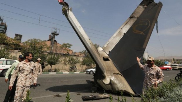 A member of the Iranian Revolutionary Guards reacts as he stands next to the remains of a plane that crashed near Tehran's Mehrabad airport on August 10, 2014. A civilian airliner crashed on take-off near the Mehrabad airport in the capital, Iranian news agencies said, with reports that almost 50 people were killed.