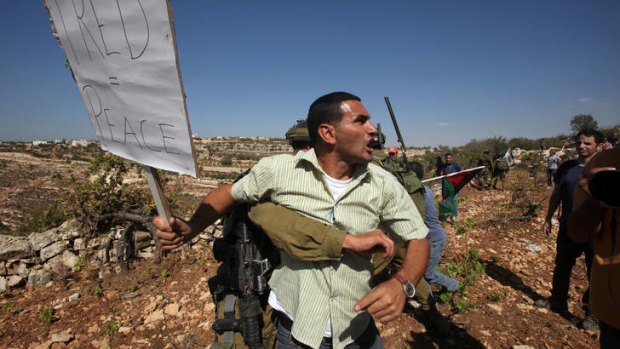 A Palestinians demonstrator is restrained by an Israeli soldier as he tries to reach Palestinian lands to pick grape and olive trees, near the fence of the Israeli settlement of Karmi Tsour, north of the West Bank town of Hebron.