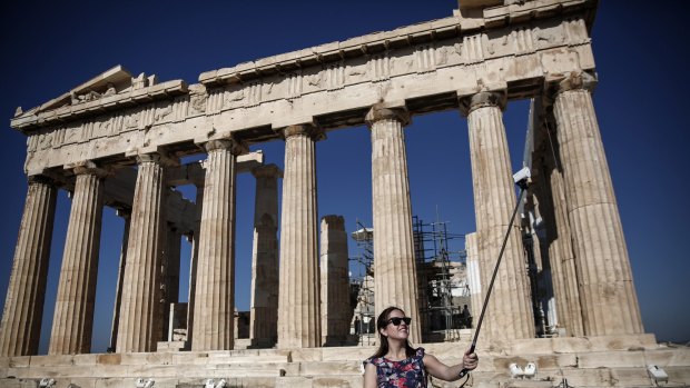 A tourist takes a selfie as she stands beside the Parthenon in Athens.