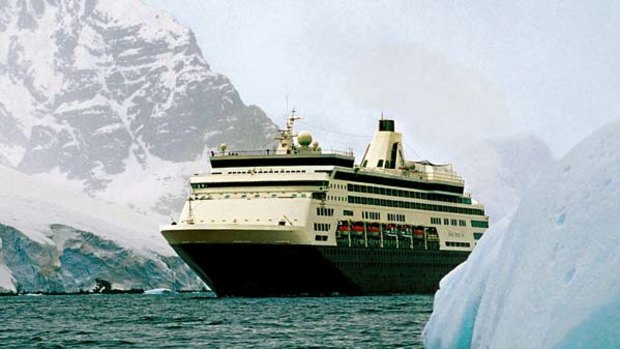 Approaching a large iceberg, a cruise ship sails through Antarctic waters.