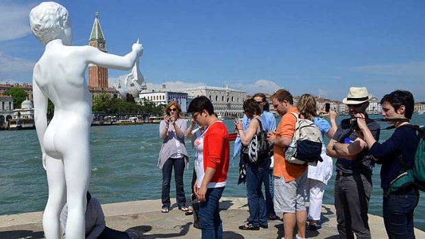 Tourists watch as technicians prepare the removal of the sculpture of a boy holding a frog in Venice.