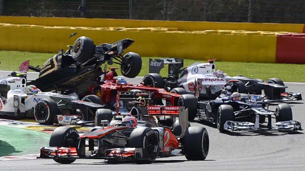 Carnage ... Jenson Button avoids trouble on turn one as Lotus driver Romain Grosjean gets airborne in the Belgian Grand Prix.