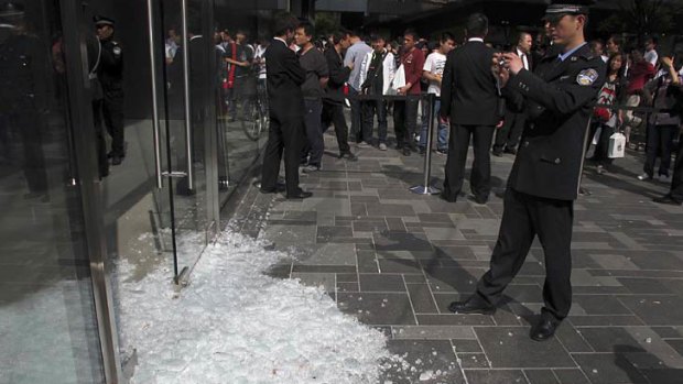 In this photo taken Saturday 7 May, 2011, a Chinese policeman takes photos of the broken glass door in the aftermath of a scuffle at Apple's Sanlitun retail store in Beijing, China.