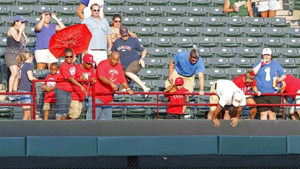 Fans in the outfield bleachers react after seeing the man fall over the rail.