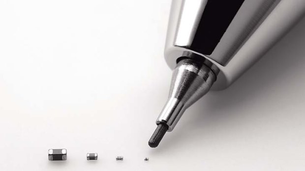 Murata's latest capacitor, measuring just 0.25 millimeter by 0.125 millimeter, right, is pointed by a mechanical pencil as it is displayed with its bigger size models.