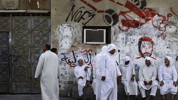 Bahraini men chat on a bench in the western village of Malkiya in front of a wall sprayed with graffiti opposing the Bahrain Grand Prix.