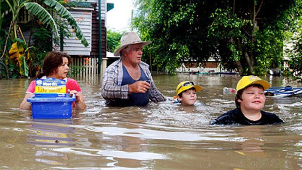 Paul Barnes and Mandy Greene with their sons, Patrick, right, and Bradley, wade through chest-high water to return to their house to find their insurance documents in Rockhampton yesterday.