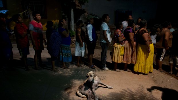 A dog lies alongside a line of people waiting to receive a plate of stewed mutton, tortillas, and rice distributed by a community group from neighboring El Espinal, in a zone heavily affected by Thursday's magnitude 8.1 earthquake in Juchitan, Oaxaca state, Mexico, Monday, Sept. 11, 2017. Numerous community, church, and municipal groups from other Mexican states, as well as from nearby towns less severely impacted by the quake, have been privately distributing food, clothes, and basic supplies to Juchitan's population. (AP Photo/Rebecca Blackwell)