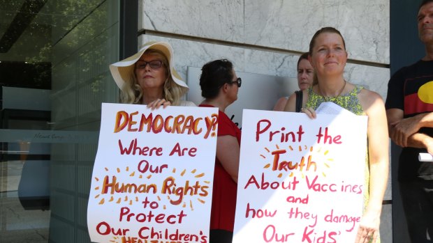 Women hold up signs criticising vaccination in Australia.