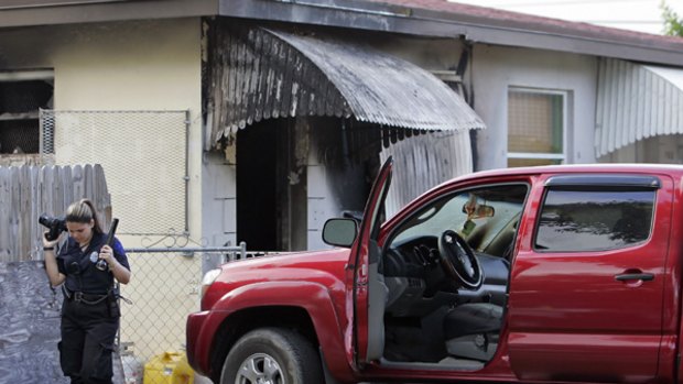 A Miami police officer photographs the burned house where a man shot himself after shooting four others at a family gathering at another location.