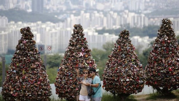 Love but less children ... A couple takes a selfie in front of trees covered with "love locks" at N Seoul Tower located atop Mount Namsan in central Seoul.