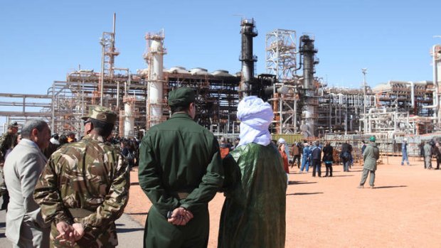 Algerian soldiers and officials stand in front of the gas plant in Ain Amenas, seen in background, during a visit organized by the Algerian authorities following the January 2013 attack directed by Moktar Belmoktar.