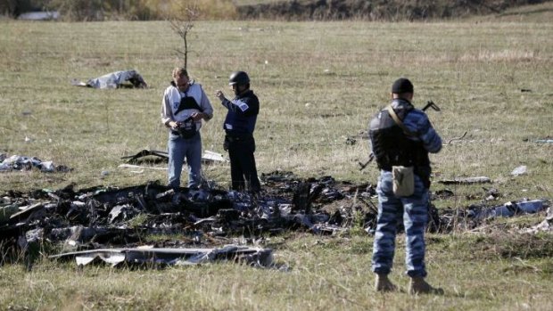 Members of the Organisation for Security and Cooperation in Europe (OSCE) stand near a policeman (right) representing Donetsk People's Republic at the crash site.