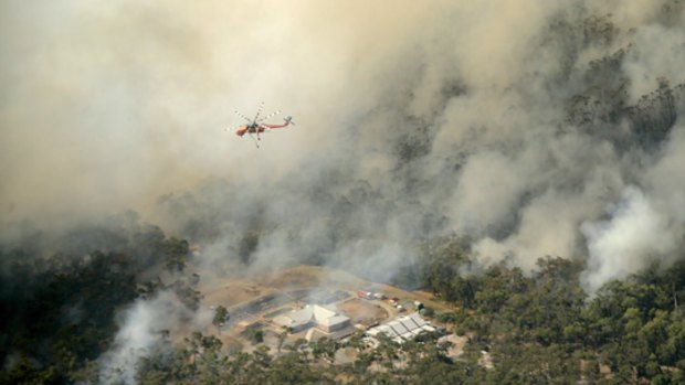 A water-bombing helicopter hovers over a Belgrave South property caught in the path of bushfires yesterday.