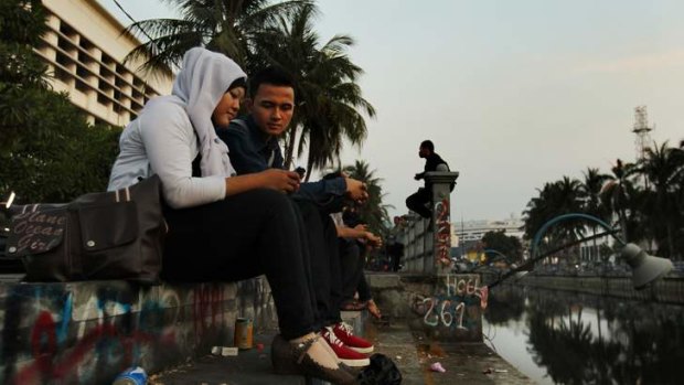 A couple sit at a canal in Jakarta's old quarter, where historic buildings await renovation.