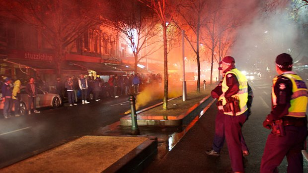 Police keep an eye on fans in Lygon Street, where smoke from flares filled the area.