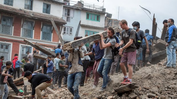 Emergency workers and bystanders clear debris while searching for survivors under a collapsed temple in Basantapur Durbar Square following an earthquake.