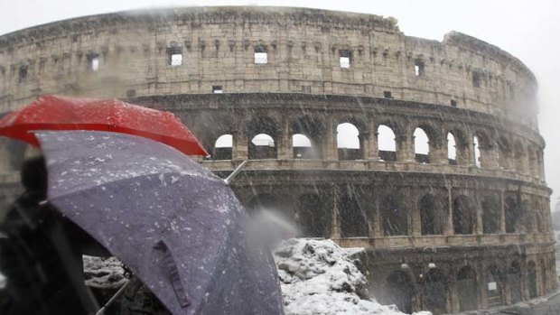 Tourists protect themselves from the falling snow with umbrellas as they view Rome's ancient Colosseum.