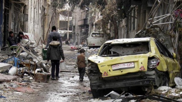 People walk past a damaged car along a damaged street in the besieged area of Homs in Syria.