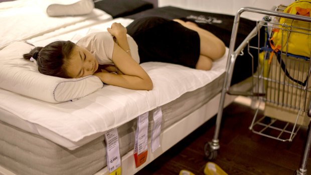People sleeping on bedroom furniture and chairs inside in IKEA Beijing Siyuanqiao Store.