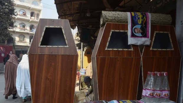 Rising trade ... A Pakistani carpenter (right) makes a coffin as pedestrians (left) walks past a workshop in Peshawar. 