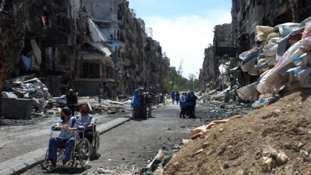 People wait to receive food supplies on a damaged street in the besieged Yarmouk refugee camp in Damascus.