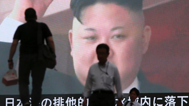 People walk past a TV screen showing an image of North Korean leader Kim Jong-un in Tokyo.