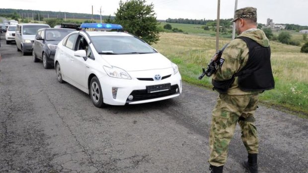 Rebel-held territory ... A man wearing military fatigue stops traffic near the site of the crash site of MH17.