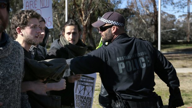 An ACT police officer pushes back some protesters who tried to get closer to the Reclaim Australia rally.  