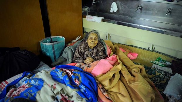 Humanitarian crisis ... an elderly woman hunkers down under blankets at an evacuation shelter in a school in Kesennuma, 70 kilometres north-east of Ishinomaki.