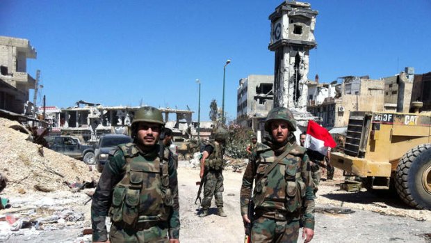 Reclaimed: Syrian government soldiers stand in front of the clock tower flying the national flag in the main square of Qusair on Wednesday.