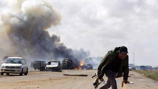 A rebel fighter runs for cover in front of vehicles belonging to loyalist forces after a coalition air strike along the road between Benghazi and Ajdabiya.
