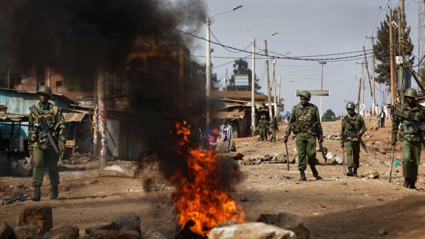 Riot police walk past burning barricades erected by protesters throwing rocks, during clashes in the Kawangware slum of Nairobi, Kenya.