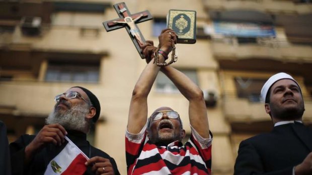 An anti-Mursi protester brandishes a cross and Koran.