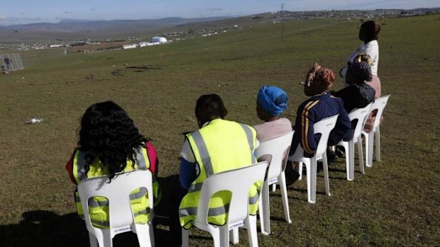 Local women sit on chairs at a public viewing point near the burial ground.