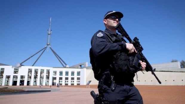 An AFP officer armed with a machine gun patrols outside the front of Parliament House.