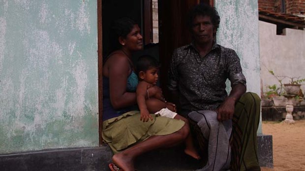 Christopher Fernando sits on the step at his single-room home in Negombo, on Sri Lanka's west coast, with his daughter-in-law Aruni and grandson Shehan.