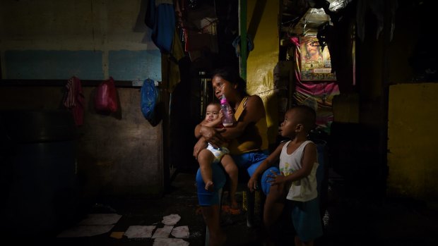 Ruth-Jane Sombrio, who is seven months pregnant, sits in front of her home with her two children. She witnessed the killing of her husband.