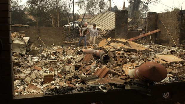 Residents in Duffy walk through the rubble of their home the day after the January 18 firestorm in 2003.