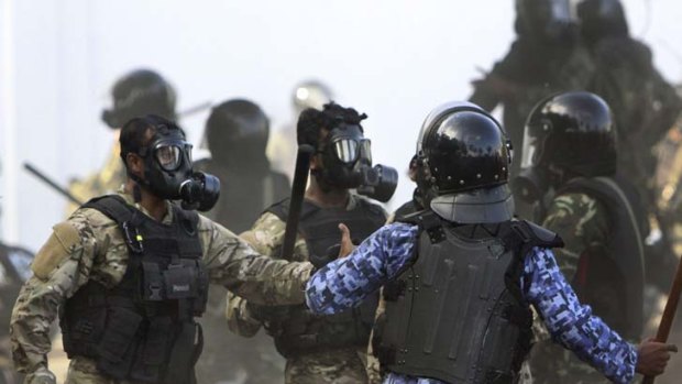 A Maldives police officer, in blue, charges soldiers during a clash in Male, Maldives.