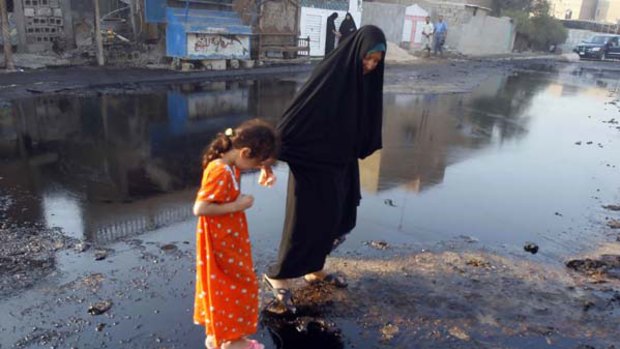 An Iraqi girl is helped by a relative as they walk on spilled oil at the spot where a fuel truck exploded in the Iraqi capital's Ur district. <i>Picture: AFP</i>