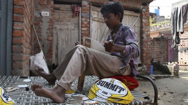 A 13-year-old boy stitches Summit rugby league balls outside his home in northern India.
