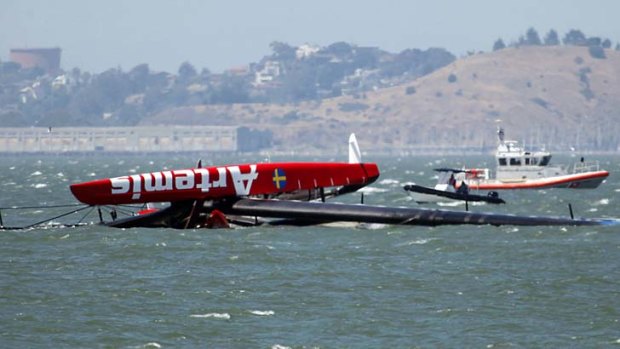 The overturned Artemis Racing AC72 catamaran is towed past Treasure Island after it capsized during training in San Francisco Bay.