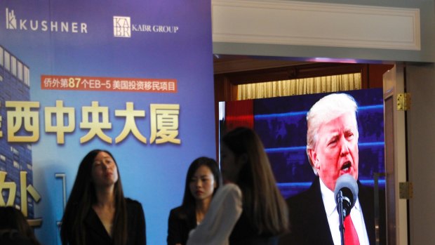 A projector screen shows footage of US President Donald Trump as workers wait for investors at a reception desk during an event promoting a Kushner Companies development, in Shanghai, China, on Sunday.