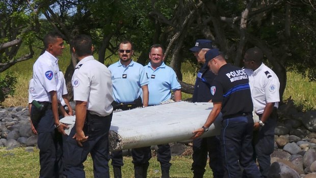 French gendarmes and police carry a piece of debris from MH370, which was found on the beach in Saint-Andre, on the French Indian Ocean island of Reunion.