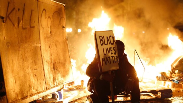 A demonstrator sits in front of a street fire during a Ferguson demonstration in Oakland, California.