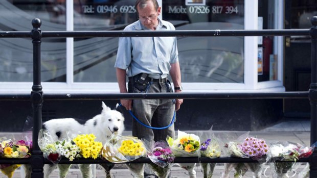 A man reads floral tributes left at a taxi rank on Duke Street, Cumbria.