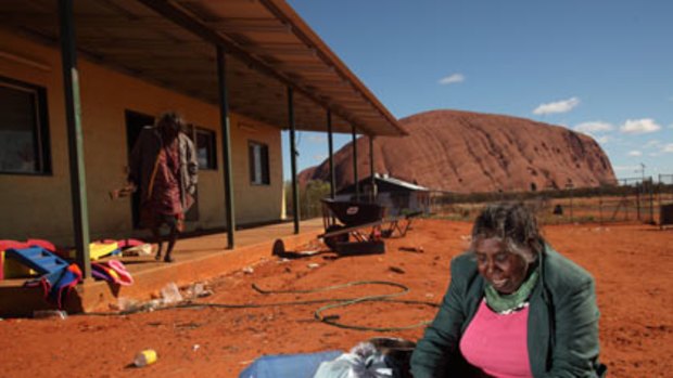 Traditional owner Judy Trigger weaves baskets for tourists with Uluru behind her.