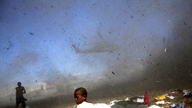 A Haitian boy shelters from the air blast from a US helicopter delivering supplies in Port-au-Prince. The Haiti government has raised the quake toll to 230,000.