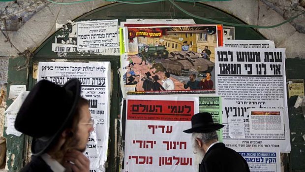 Ultra-Orthodox Jewish men walk past a poster in the Jewish Mea Shearim neighborhood in Jerusalem. A large cartoon poster depicts Haredi soldiers rolling through the streets atop tanks trying to lure young boys onto their vehicles.